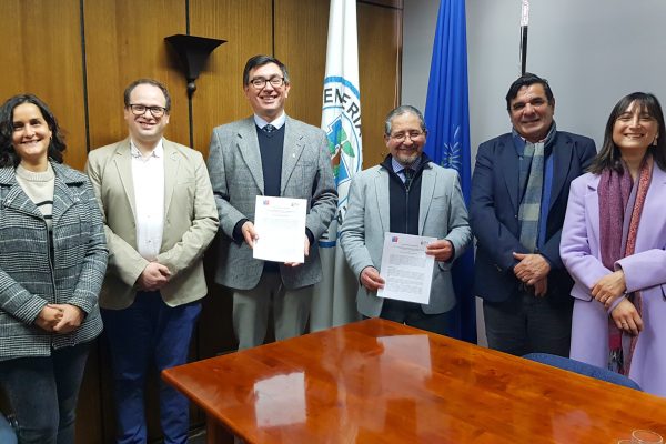 Asistentes a firma del convenio miran hacia el frente y las autoridades sostienen el convenio en sus manos.