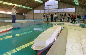 Profesional del instituto ante buques del modelo a escala del Puerto San Antonio, explicando sobre la instalación a las personas presentes.